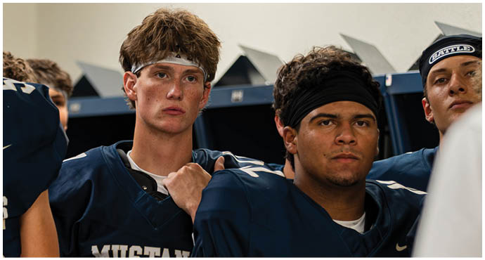Three football players in blue and white uniforms running on a field. Description generated by AI