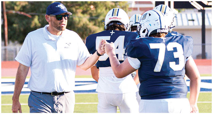 Three football players in blue and white uniforms running on a field. Description generated by AI