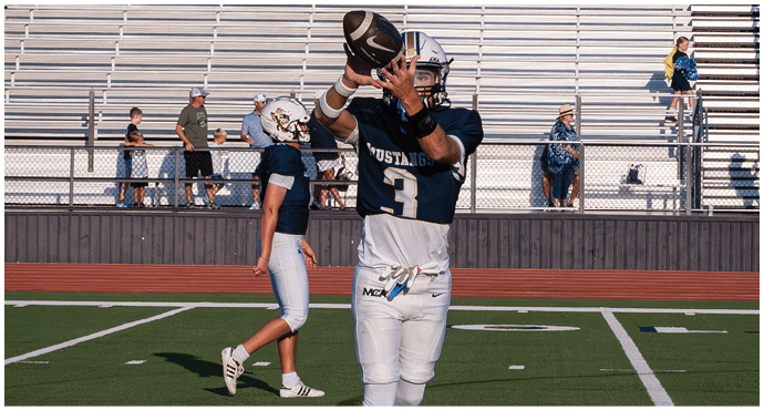 Three football players in blue and white uniforms running on a field. Description generated by AI