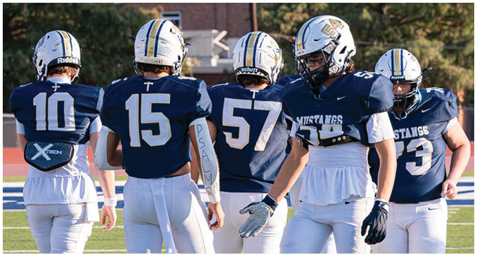 Three football players in blue and white uniforms running on a field. Description generated by AI