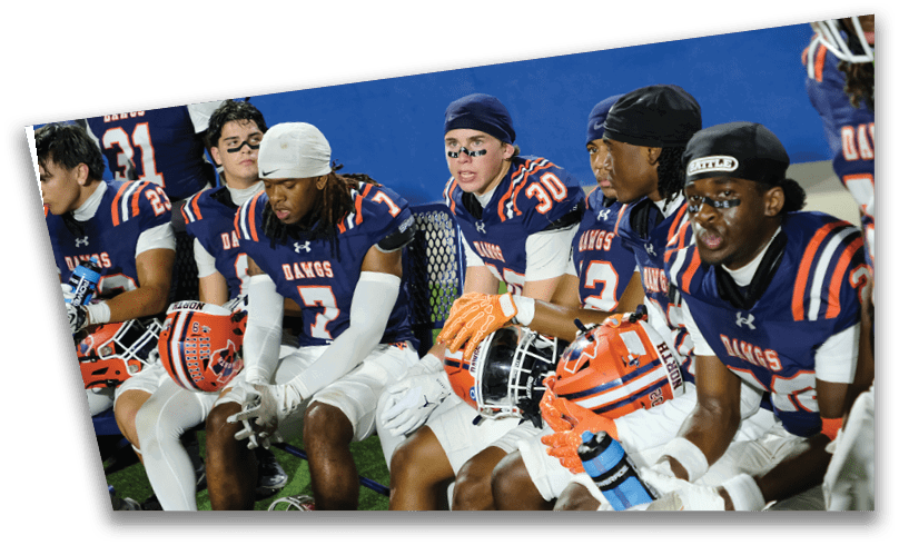 People wearing black American Canyon football uniforms and helmets are standing on a football field at night. Description generated by AI