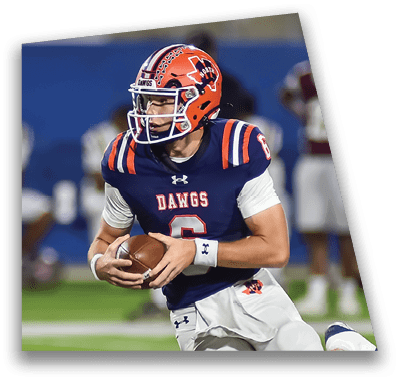 A person in football gear and helmet is crouched on a field with other players lined up in the background during a game. Description generated by AI