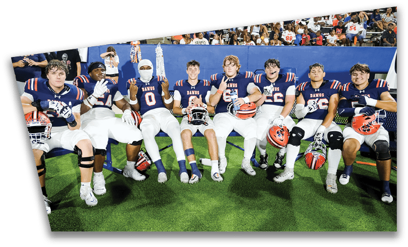 People wearing black American Canyon football uniforms and helmets are standing on a football field at night. Description generated by AI