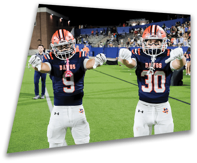 Four people in dark football uniforms and helmets stand in a row on a field, appearing focused and ready for action. Description generated by AI