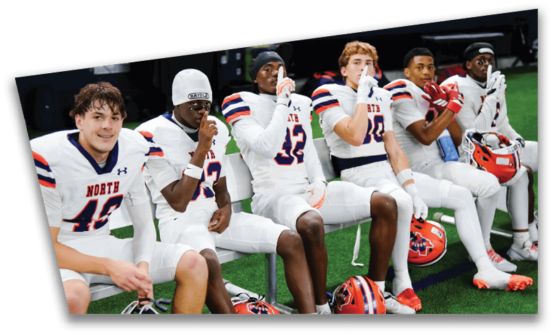 People wearing black American Canyon football uniforms and helmets are standing on a football field at night. Description generated by AI