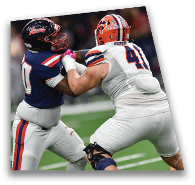 A person in football gear and helmet is crouched on a field with other players lined up in the background during a game. Description generated by AI