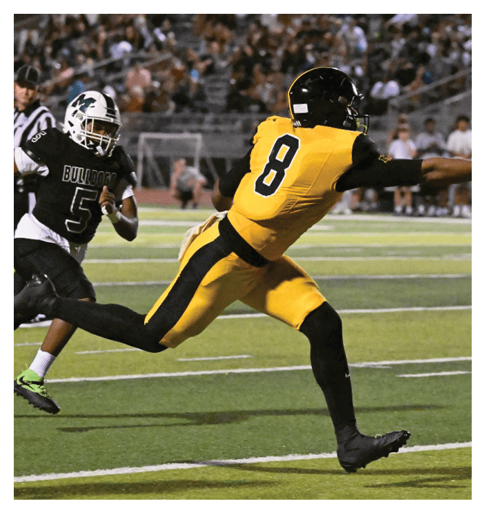A football game is in progress with players on the field. One player is throwing a football while another player is trying to catch it. The players are wearing uniforms and are actively engaged in the game. AI generated content