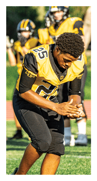 A football player is kneeling on the field, wearing a green jersey and a helmet. AI generated content