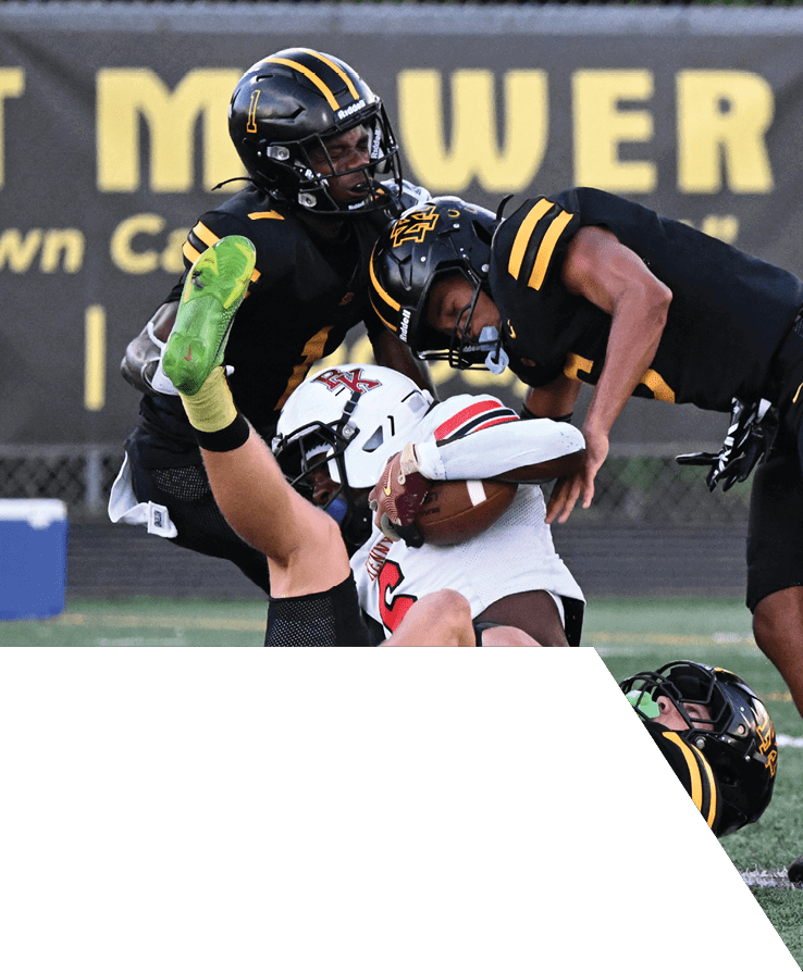 Two people in football uniforms are engaged in a tackle on a grassy field during a game. Description generated by AI