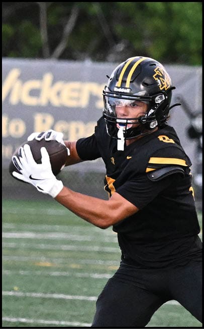 A person in a black and yellow football uniform is catching a football on a green field with yard lines. Description generated by AI