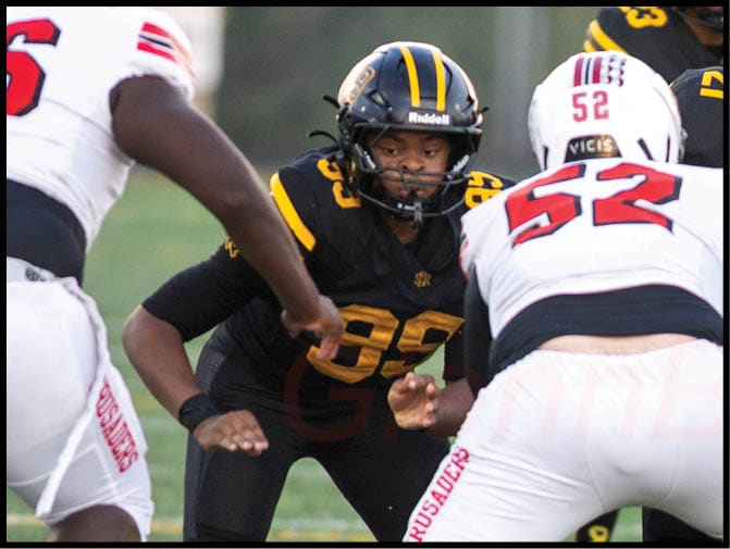 Two people in black and yellow football uniforms face two people in white and red football uniforms on a field during a game. Description generated by AI