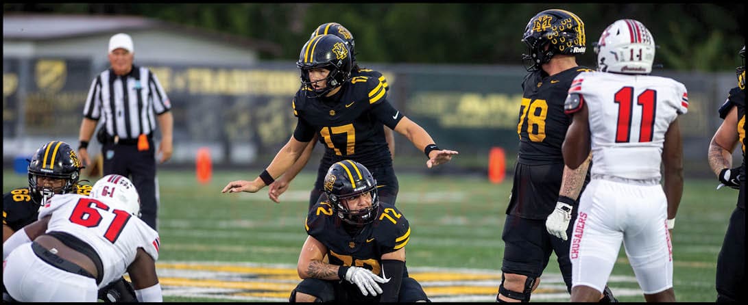 People in football uniforms are positioned on a field preparing for a play during a game. Description generated by AI