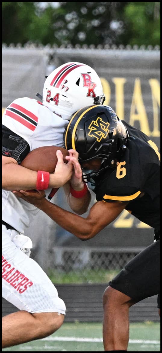Two people in football uniforms are engaged in a close physical tackle on a field, with one holding a football. Description generated by AI