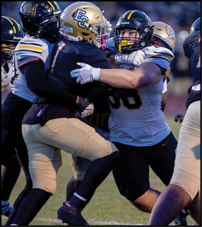 Two football players in helmets and uniforms are engaged in a physical struggle on the field during a game. Description generated by AI