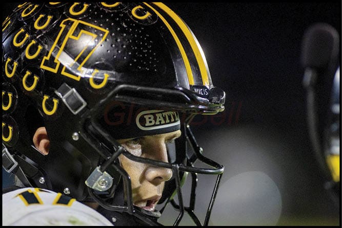 A person wearing a black football helmet with yellow horseshoe logos and the number 17 is focused and ready during a nighttime game. Description generated by AI