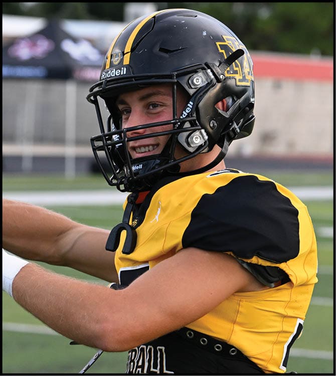 A person wearing a black and yellow football uniform and helmet is preparing to throw a football on a field. Description generated by AI
