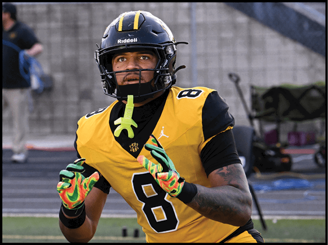 A person wearing a yellow and black football uniform with the number eight is on a field, appearing focused and ready to catch or receive a ball. Description generated by AI