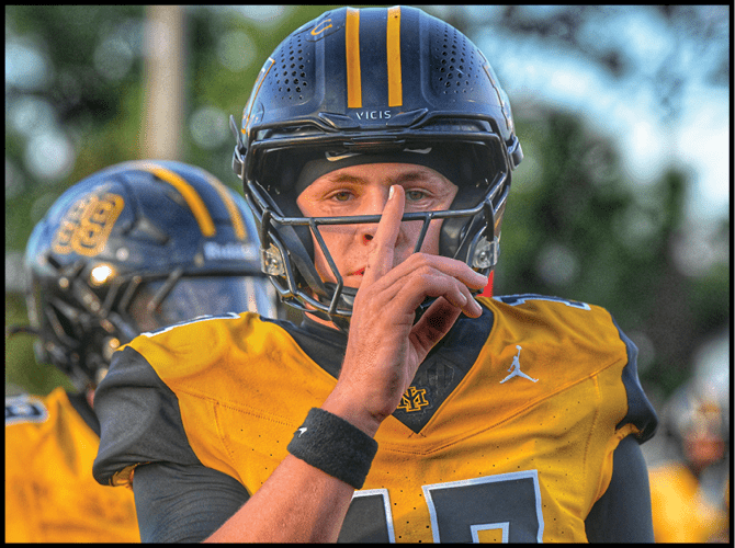 A person wearing a yellow and black football uniform and helmet is holding a finger to their lips in a shushing gesture. Description generated by AI