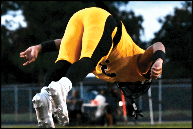 A person wearing a yellow and black sports uniform is bent over, possibly participating in an athletic activity outdoors. Description generated by AI