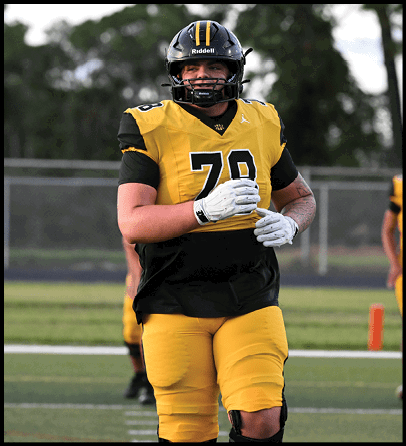 People wearing yellow and black football uniforms standing on a field with a blurred background. Description generated by AI