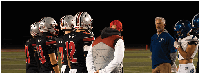 Several people in football uniforms and casual clothing stand on a field at night, appearing to discuss or observe something. Descripci n generada con IA