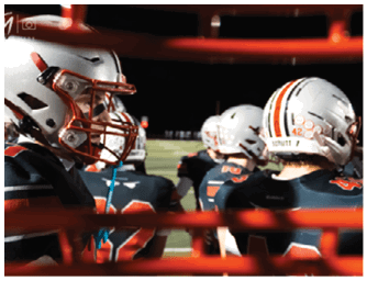 Several people wearing football helmets and uniforms are standing together on a field at night. Descripci n generada con IA