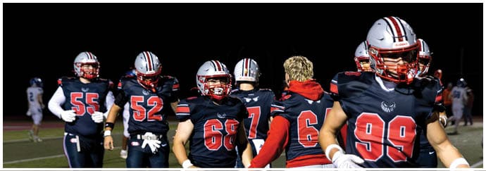 A group of people wearing football uniforms and helmets are standing on a field at night. Descripci n generada con IA