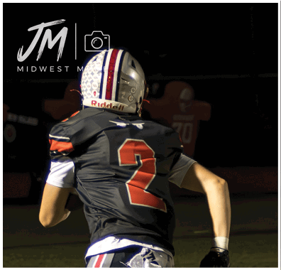 Two people in football uniforms are running on a field during a nighttime game. Descripci n generada con IA