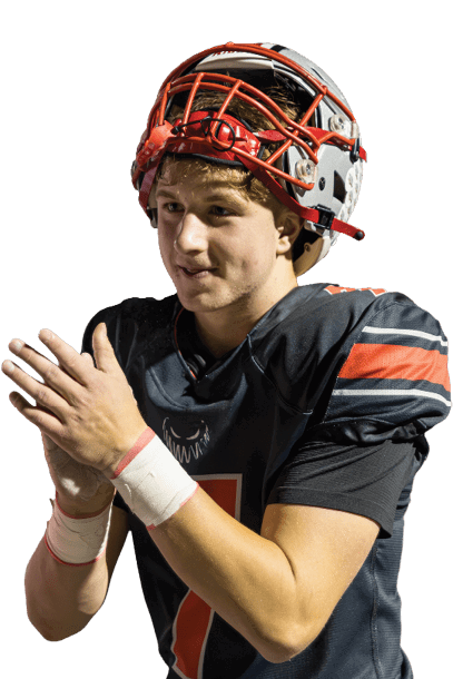 A person wearing a football helmet and uniform is clapping their hands on a sports field at night. Descripci n generada con IA