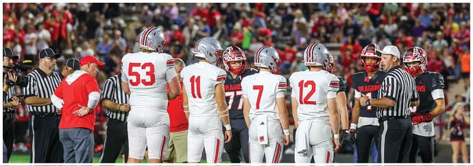 A group of football players in white and red uniforms and referees are gathered on the field with a crowd of spectators in the background. Descripci n generada con IA