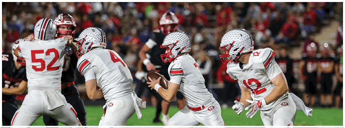 Four people in white football uniforms are actively engaged in a play on a grassy field during a game. Descripci n generada con IA