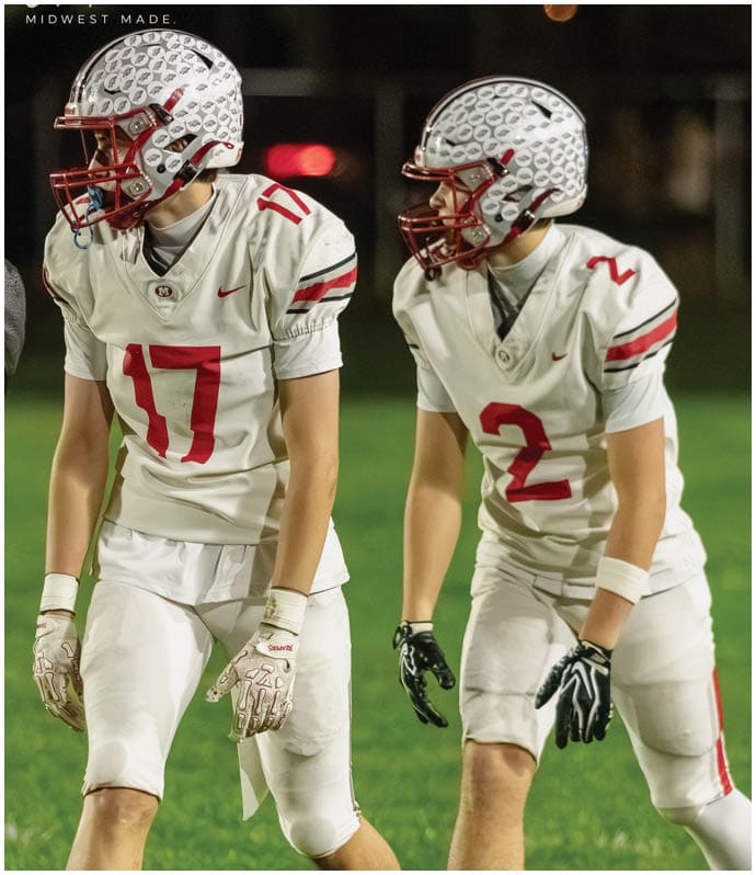 A person wearing a white football jersey with the number 2 and a white helmet with a red faceguard is looking to the side on a football field at night. Descripci n generada con IA
