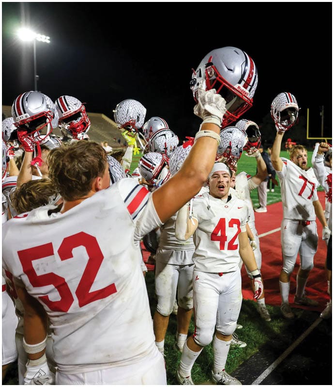 Football players in white uniforms and cheerleaders with pom-poms celebrate enthusiastically on a field at night. Descripci n generada con IA