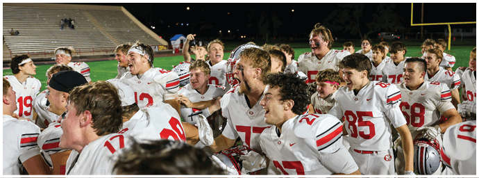 A group of people wearing sports uniforms are celebrating together on a field at night with empty bleachers in the background. Descripci n generada con IA