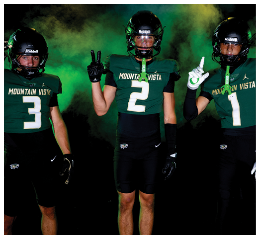 Two people wearing Mountain Vista football uniforms with helmets and gloves pose against a dark background with green smoke, one holding up three fingers and the other holding up two fingers. Description generated by AI
