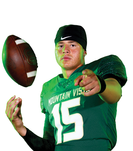 A person wearing a green football jersey with the number 15 and black athletic pants is tossing a football while pointing forward. Description generated by AI