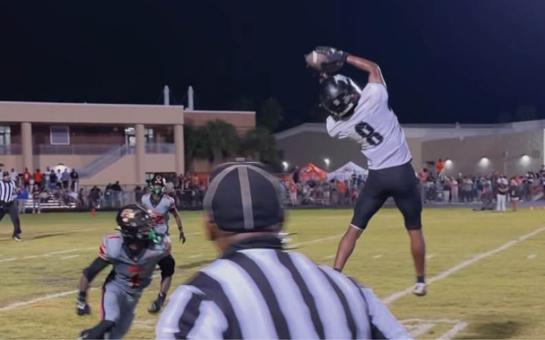 A person wearing a football uniform with the number 8 is jumping and reaching up to catch a football during a nighttime game. Description generated by AI