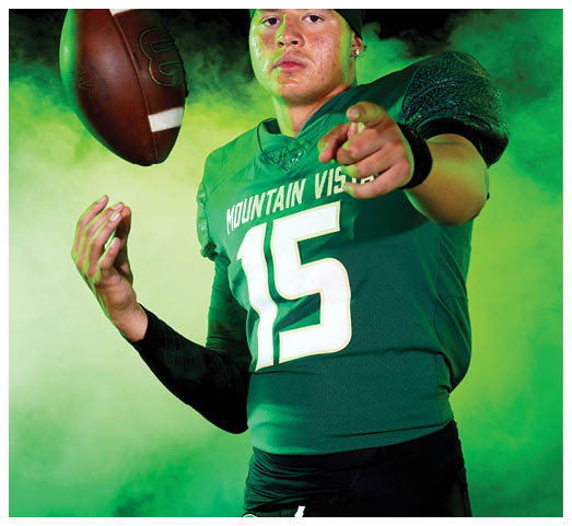 A person wearing a green football jersey with the number 15 and a black headband is throwing a football against a smoky green and black background. Description generated by AI