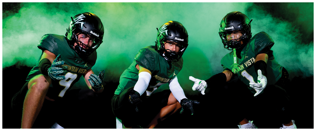 Three people wearing green football uniforms and helmets pose energetically against a smoky green and yellow background. Description generated by AI
