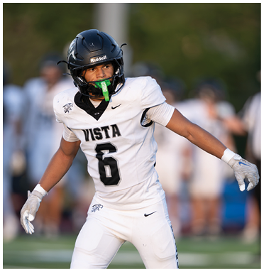 A person wearing a black helmet and a white football jersey with the number six and the word Vista is on a field, appearing focused and ready for action. Description generated by AI