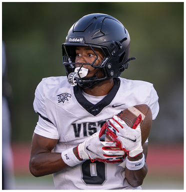 A person wearing a white sports jersey with the number zero is holding a red and white football while wearing white gloves. Description generated by AI