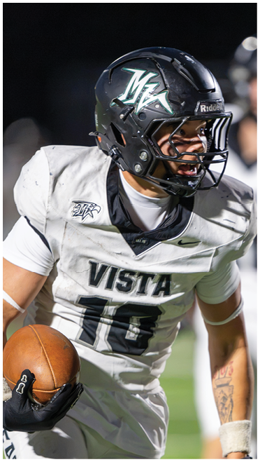 A person wearing a white football uniform with the word Vista and the number 16 is holding a football while running on a field. Description generated by AI