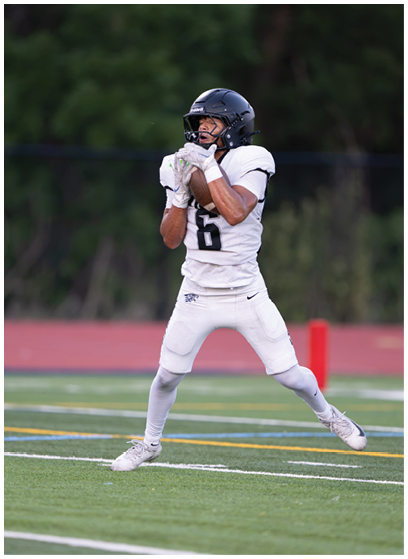 A person wearing a white football uniform and helmet is catching a football on a grassy field. Description generated by AI