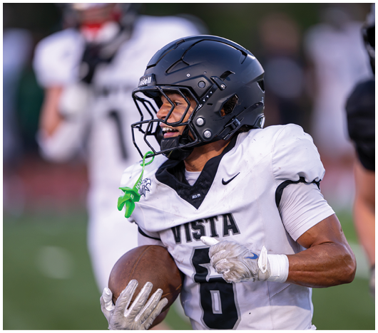 A person wearing a black helmet and a white football jersey with the word “VISTA" is on a sports field. Description generated by AI