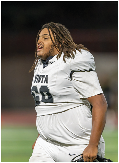 A person wearing a white football uniform with the number 69 and holding a helmet is standing on a field. Description generated by AI