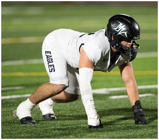 A person wearing white football pants with the word “EAGLES" printed on the side is crouched on a green field. Description generated by AI