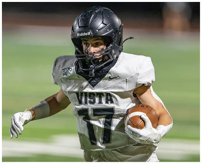 A person wearing a black helmet and white football uniform with the number 17 is running on a football field while holding a football. Description generated by AI