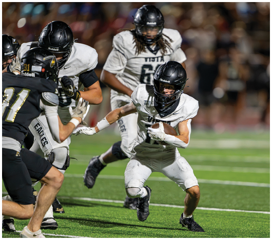 Several people in football uniforms are actively engaged in a play on a green field during a game. Description generated by AI