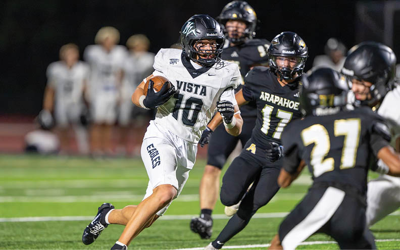 A person in a white football uniform with the number 10 is running with the ball while being chased by several people in black football uniforms on a field. Description generated by AI