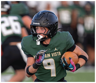 A person wearing a green football uniform with the number nine and a black helmet is running while holding a football on a field. Description generated by AI